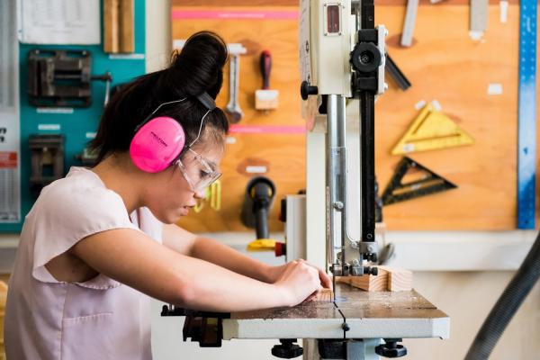 Trang L. uses the band saw with proper eye and ear protection, which is an important part of makerspace safety.