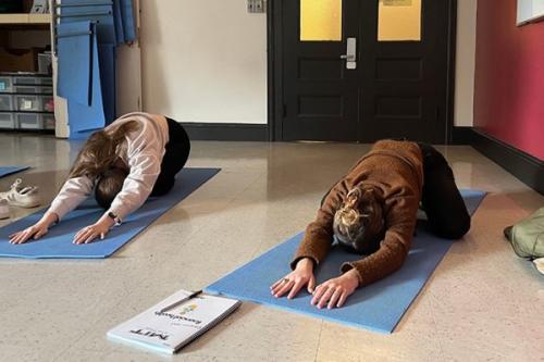 Two MIT students perform the child's pose in a yoga class.